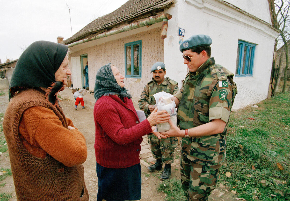 A Pakistani peacekeeping soldier distributing food to an elderly woman. (UN)